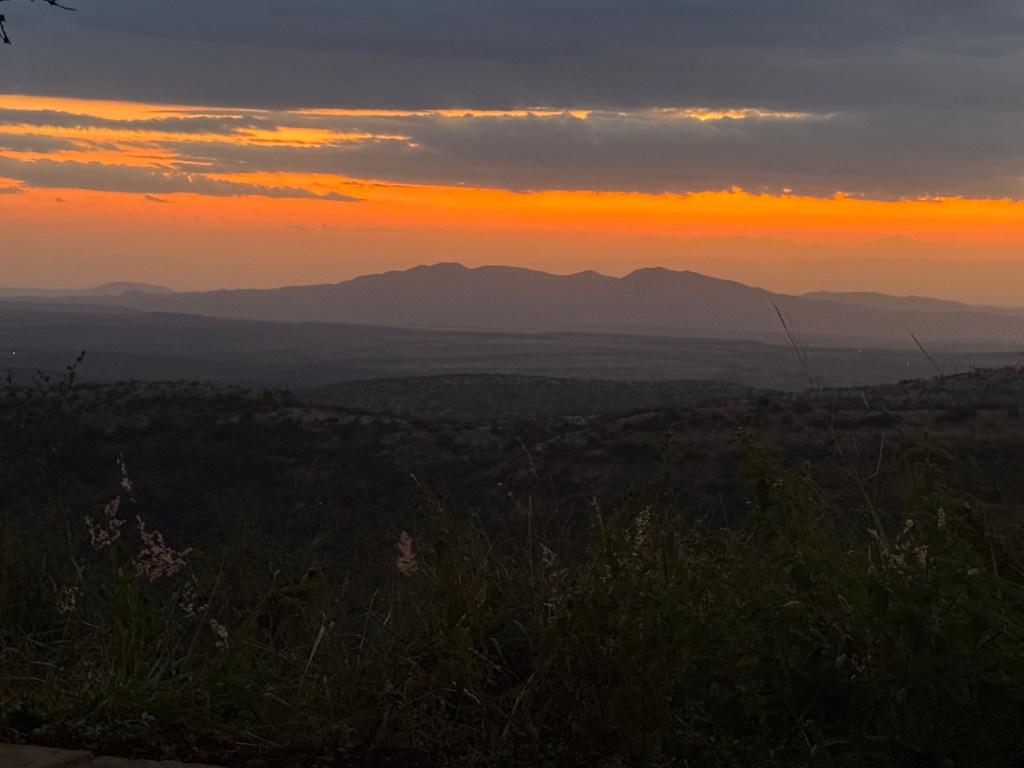 A scenic view of a sunset over rolling hills, with vibrant orange and yellow hues in the sky, capturing the tranquil beauty of the landscape.